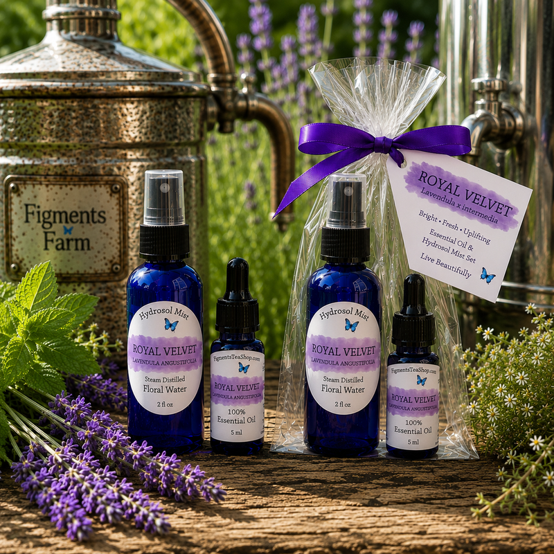 Three cobalt blue essential oil bottles with purple and white labels are arranged on a wooden surface outdoors. Two small bottles are shown individually, and one larger bottle is wrapped in clear cellophane with a purple ribbon and a product tag reading Royal Velvet.