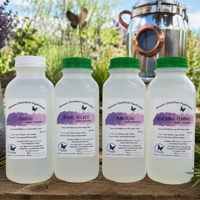 Four bottles of steam distilled herbal tinctures lined up on a wooden surface with a copper distillation pot and green foliage in the background. The bottles have white plastic bodies, white caps, and green caps on three of the bottles, and feature purple watercolor-style labels with the names Grosso, Royal Velvet, Tunstead, and Riverina Thomas.